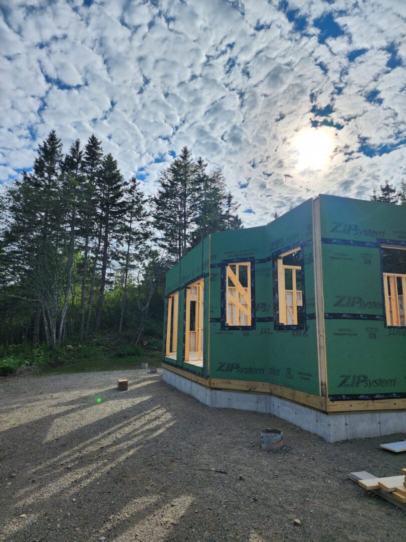 A green building under construction with trees in the background.