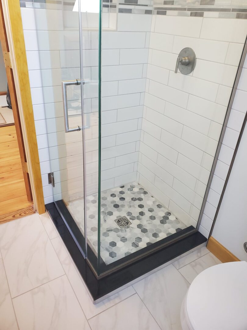 A bathroom with a glass shower door and tile floor.