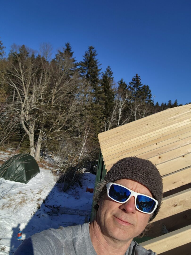 A person with sunglasses and hat standing in the snow.