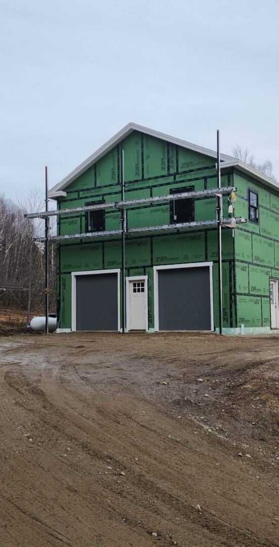 A green building with two garage doors and scaffolding around it.