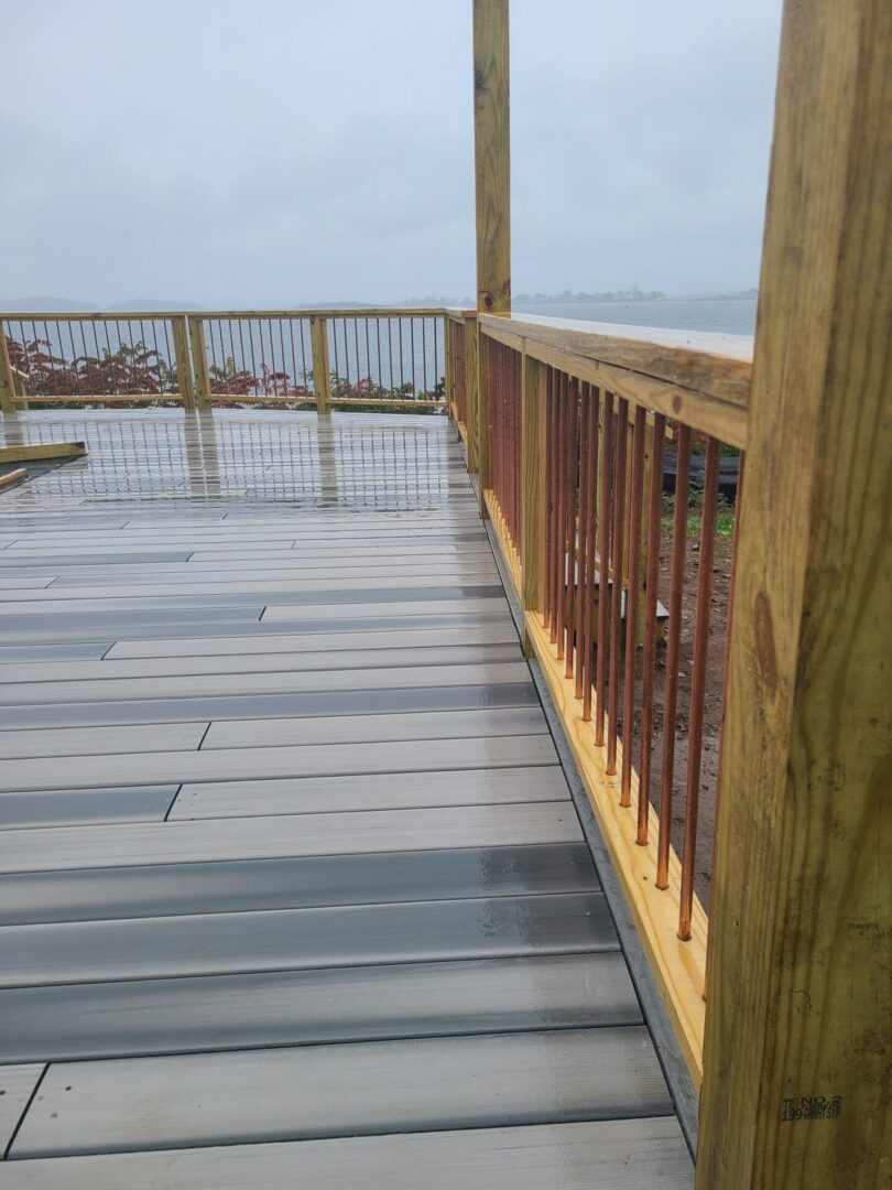 A wooden deck with metal railing and water in the background.